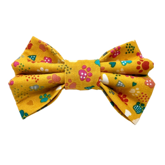 Yellow bow tie with colourful paw patterns on a white background