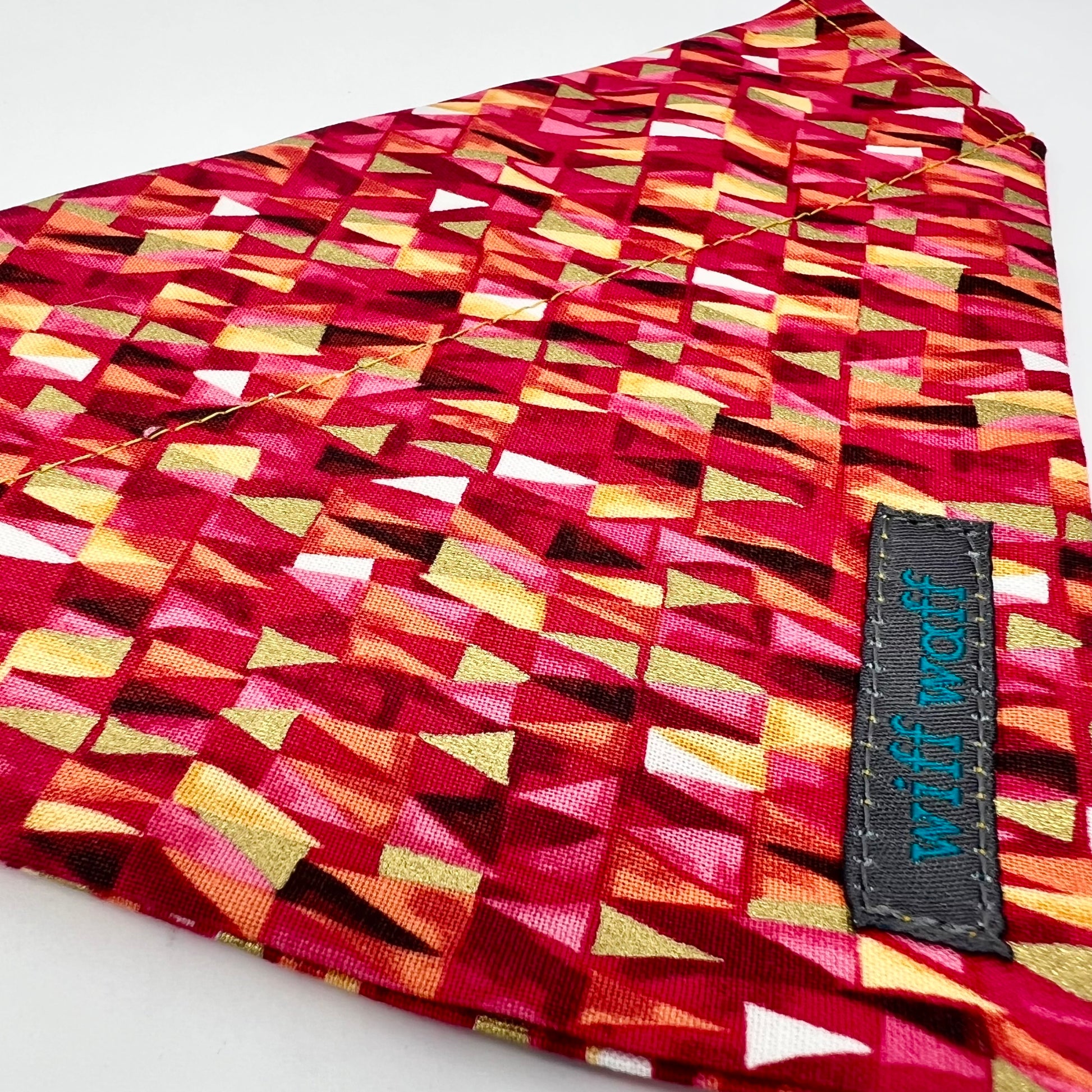 A dog collar bandana featuring pink and red hues accented with gold metallic touches