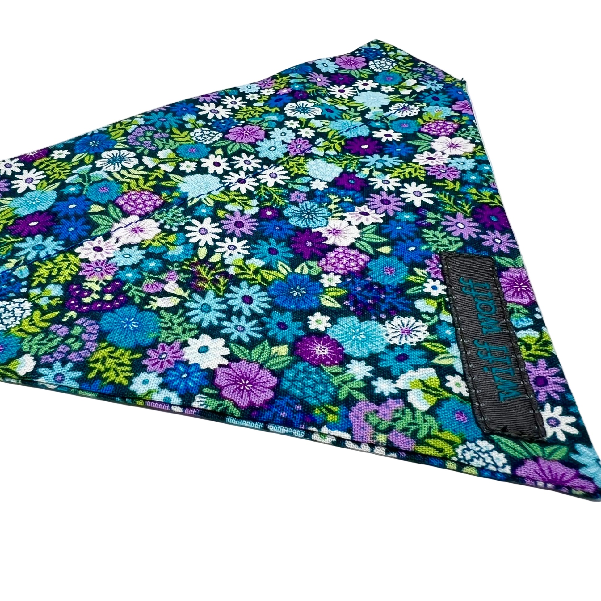 a dog collar bandana features a vibrant floral design in shades of blue, violet, green and white, giving it a refreshing look.