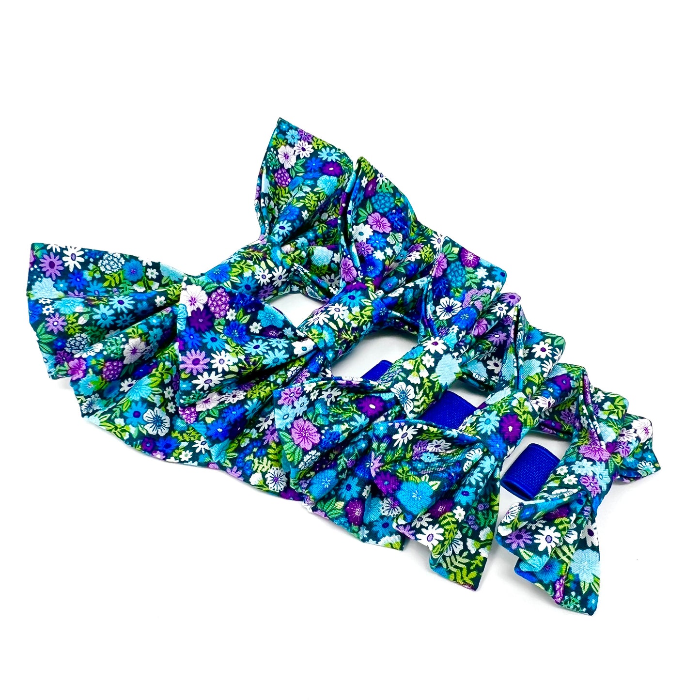 Five colourful dog bows featuring a vibrant floral design in shades of blue, violet, green and white. Sizes small. medium, large, large plus and small XL.