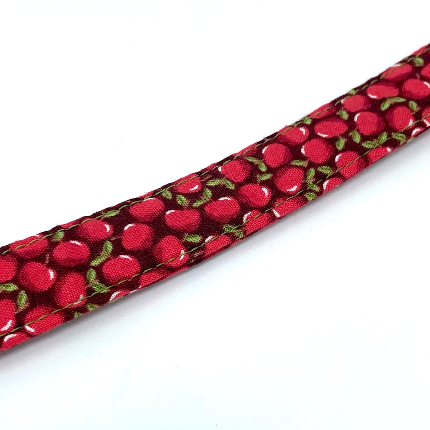 A close up image of a handcrafted fabric dog lead handcrafted by wiff waff designs in nottingham. Red apple print fabric dog lead on a dark background with green stitching.